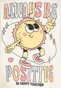 Grafische t-shirt met een cartoon zon met grote ogen, die roze sneakers draagt, omringd door kleurrijke tekst en sterren op een lichte achtergrond.