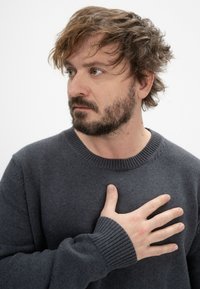 Dunkelgrauer Strickpullover mit gerippten Bündchen und Halsabschluß, getragen von einer Person mit Bart, die Hand über der Brust gelegt, strukturierter Stoff sichtbar.