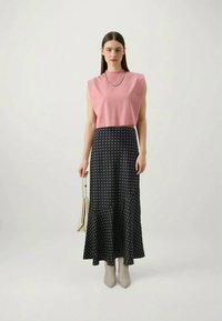 Un haut sans manches rose associé à une jupe midi à pois noirs, avec un ourlet évasé. La tenue est complétée par des bottes à talons beiges.