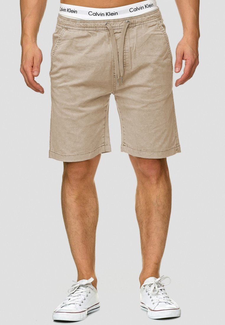 Beige puuvillashortsit, joissa on elastinen vyötärö ja nauhakuja, sivutaskut ja suora lahje. Yhdistetty valkoisiin lenkkareihin.