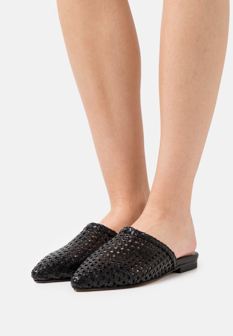 Mules tissées noires avec un bout pointu et un talon plat, fabriquées en matériau texturé avec un dos ouvert.