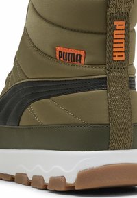 Olīvu zaļas augstās tenisa kurpes ar melniem akcentiem, teksturētu audumu un baltu zoli. Sānos ir izteikts oranžs Puma logo.