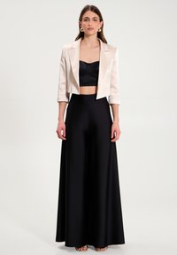 Cremesatin kurzes Blazer über einem schwarzen Satin-Crop-Top und hochtaillierten schwarzen weiten Hosen. Glatte Texturen, minimale Akzente, eleganter Schnitt.
