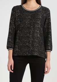 Schwarzer Pullover mit glitzernder Textur, runder Ausschnitt und Dreiviertelärmel. Mit einem gestreiften Saum akzentuiert.