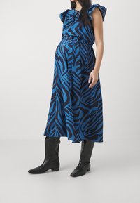 Sinivalkoinen seeprakuosinen midi-mekko, jossa on liehuttavat hihat, vyötäröltä vyötetty, ja laskeutuva kangas; yhdistetty mustiin polven yli ulottuviin saappaisiin.