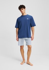 T-shirt in cotone blu navy con scollatura a girocollo e logo, abbinata a pantaloni corti a righe orizzontali bianchi e blu navy, con una vestibilità rilassata.