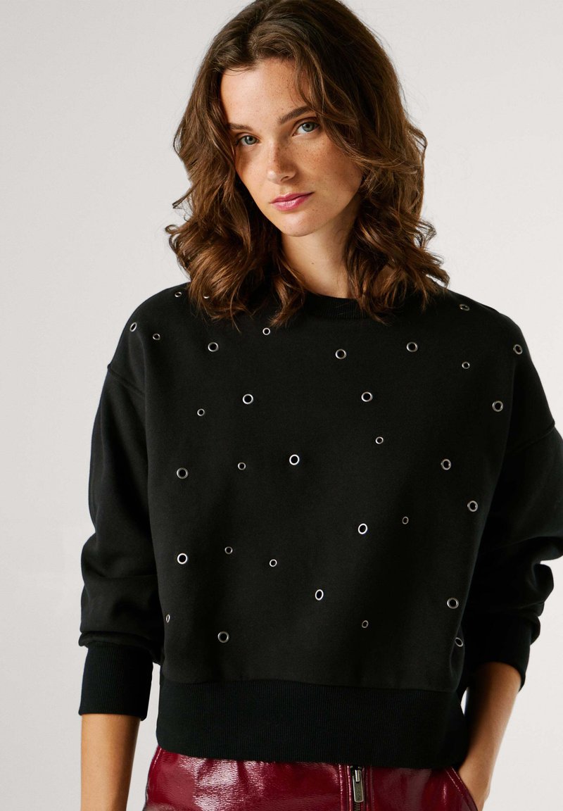 Sweat-shirt noir avec détails oeillets argentés, col rond et poignets côtelés. Tissu doux avec une coupe décontractée et aucun logo visible.