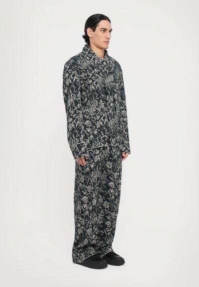 Conjunto de loungewear cu patterned realizat dintr-un material închis la culoare cu desene florale albe; include o cămașă cu guler și pantaloni largi, asortați cu pantofi negri.