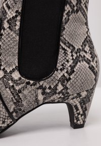 Gros plan sur une botte de cheville à petit talon avec un panneau latéral élastique noir et une texture en imprimé serpent gris sur le dessus.