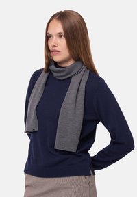 Gray scarf made of soft knit fabric, featuring a ribbed edge. Worn with a navy sweater, showcasing a relaxed drape and smooth texture.