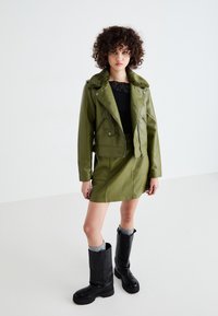 Green leather motorcycle jacket with a shearling collar, paired with a matching leather mini skirt and black knee-high boots.
