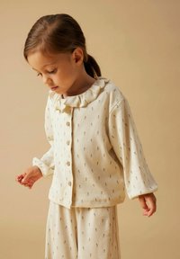 Crèmekleurige geribbelde loungewearset met een gerimpelde kraag, knoopsluiting aan de voorkant en kleine bloemenpatronen. Lange mouwen en relaxed-fit broek.