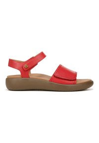 Red leather sandal with adjustable ankle strap, flat brown sole, and wide toe strap. Includes a circular gold accent on the side.