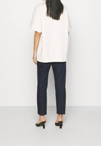 Överdimensionerad krämfärgad t-shirt med korta ärmar, parat med marinblå skräddarsydda byxor. Svarta klackmules fulländar outfiten. Slät textur, minimalistisk design.