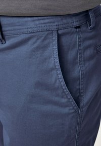 Blue textured pants with a smooth finish, featuring slanted front pockets and contrasting stitching along the waistband.