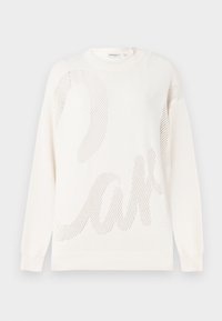 Vit stickad tröja med ett stort nätmönster som liknar ordet "cake." Ribbat halsringning och ärmslut; mjuk textur.