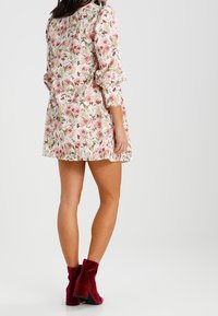 Robe fleurie avec des motifs roses et blancs, manches trois-quarts et coupe ample. Associée à des bottines bordeaux foncé.