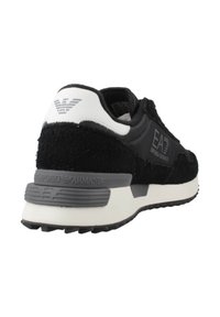 Zapatilla negra y gris con parte superior de tela texturizada, suela de goma y un talón blanco en contraste. Presenta una marca y una suela acolchada.