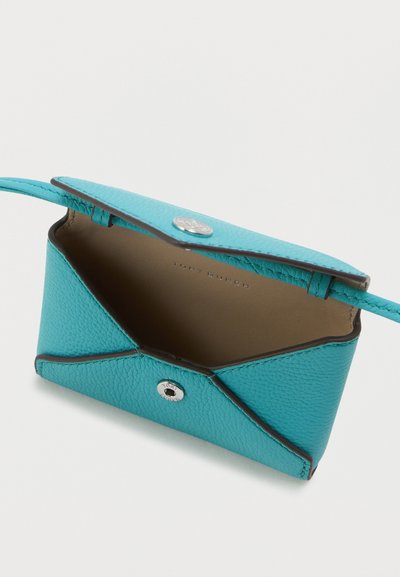 Tyrkysová kožená kabelka s textúrovaným povrchom, so zapínaním na klip a čiernym lemovaním. Interiér je béžový s embosovaným brandingom.