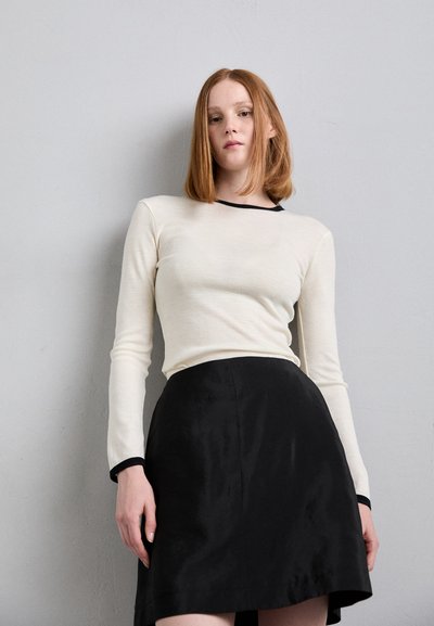 Lange mouwen, crèmekleurig shirt met zwarte halslijn en manchetten, gecombineerd met een zwarte, vloeiende A-lijn rok, gladde textuur.