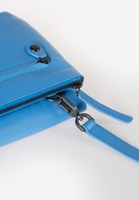 Blaues Leder-Handtasche mit glatter Textur, ausgestattet mit einem Reißverschluss, schwarzem Beschlag und verstellbarem Tragegurt. Akzentuiert mit Stichdetails.