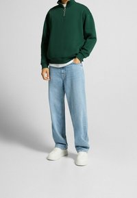 Grön halvdraget sweatshirt med ribbade ärmslut, parat med ljusblå vida jeans och vita sneakers. Slät tyg med avslappnad passform.