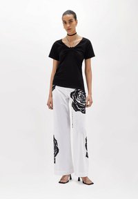 Top nero a maniche corte con design annodato, abbinato a pantaloni bianchi a gamba larga con grandi stampe di rose nere, completato con tacchi neri.