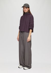 Lila gestreepte cropped hoodie met een trekkoord, gecombineerd met hoge grijze wijde broek en sneakers met witte accenten.