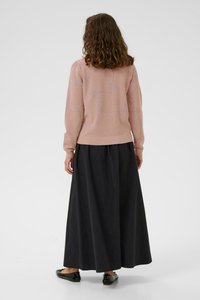 Rosa gestrickter Pullover mit einem strukturierten Muster, kombiniert mit einem langen schwarzen Rock. Das Outfit zeichnet sich durch eine lockere Passform und schlichte schwarze Schuhe aus.