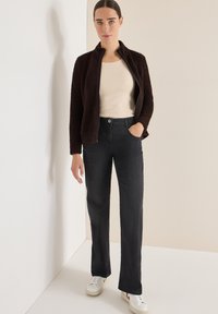 Hnědá fleece bunda s vysokým límcem, béžové přiléhavé tričko a černé džíny s rovnými nohavicemi, doplněné bílými teniskami. Jednoduchý design.