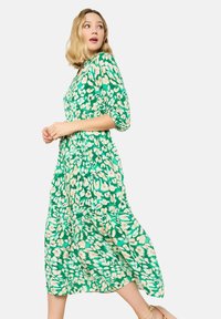 Abito midi floreale verde con maniche a sbuffo, vita aderente e gonna fluente. Il motivo presenta fiori bianchi e beige su uno sfondo vivace.