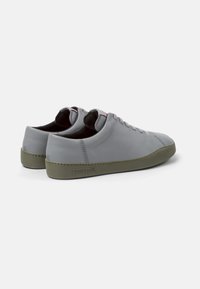 Sneaker in pelle grigia con una superficie liscia, suola in gomma verde e dettagli di cucitura sottili. La linguetta presenta un accento con logo rosso.