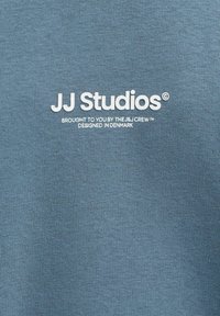 Mėlynos spalvos, minkšto ir tekstūruoto audinio džemperis su baltu užrašu: „JJ Studios“, „Pateikta J.Crew“ ir „Sukurta Danijoje“.