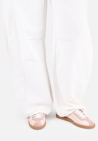 Sneakers med en ljusrosa och beige färgpalett, med en mocka-textur, vita snören och en beige gummisula. Vida, vita byxor.