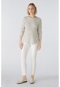 Hellgrauer, gerippter Pullover mit langen Ärmeln, kombiniert mit schmal geschnittenen weißen Hosen und beigen Loafers. Einfaches Design mit Rundhalsausschnitt.