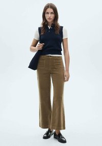 Marine gebreide vest over een witte blouse met kraag, gecombineerd met wijde, bruine corduroy broek en zwarte loafers. Eenvoudig, gestructureerd ontwerp.
