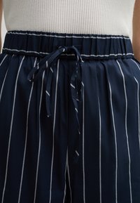Pantaloni a righe blu navy con elastico in vita e dettaglio con laccetto. Tessuto morbido con righe verticali bianche e vestibilità comoda.
