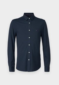 Camisa azul marino con botones, patrón de espiga, mangas largas y botones blancos. Pequeño detalle de logo en el pecho. Material de algodón.