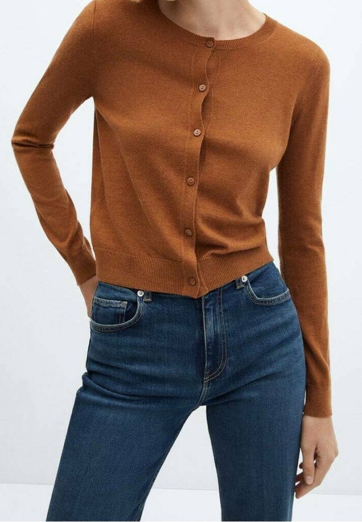 Femme portant un cardigan brun ajusté à manches longues boutonné, associé à un jean taille haute bleu foncé, sur fond clair uni.