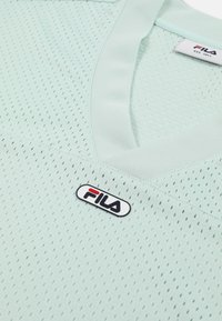 Chemise de sport perforée vert clair avec un col en V et un patch logo Fila sur la poitrine.