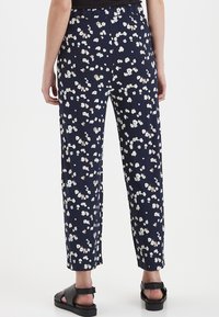 Marina blommiga byxor med avslappnad passform, elastisk midja och små vita och beige blommor. Bärs med svarta sandaler.