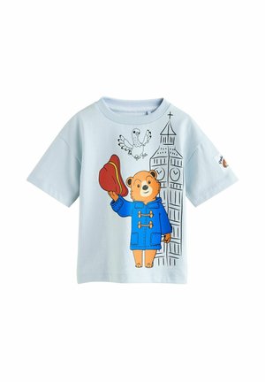 Tricou din bumbac albastru deschis, cu un urs într-un palton albastru, ținând o pălărie roșie, cu designuri grafice ce înfățișează un turn cu ceas din Londra și o pasăre zburând.