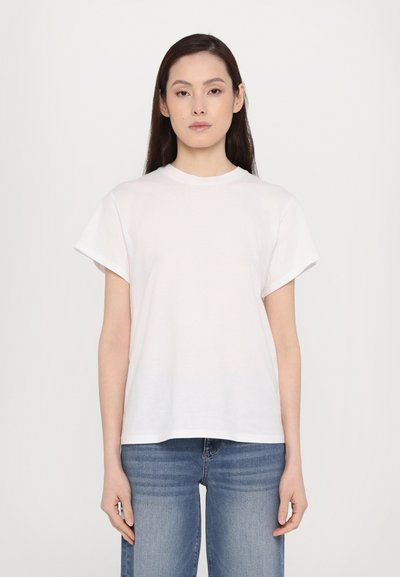 White short-sleeve t-shirt with a crew neckline, made from soft cotton fabric. Model wears blue straight-leg jeans.
