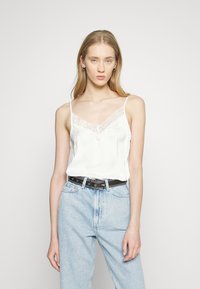 Witte satijnen camisole met kant langs de halslijn, dunne spaghettibandjes en een losse pasvorm, gecombineerd met lichtblauwe hoge taille jeans.