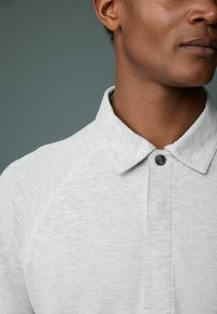 Light gray textured polo shirt with a collar, featuring a single button closure and raglan sleeve design.