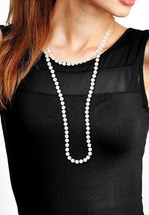Collier long en perles composé de perles blanches, présentant deux fils de longueurs variées, porté sur un haut sans manches noir.
