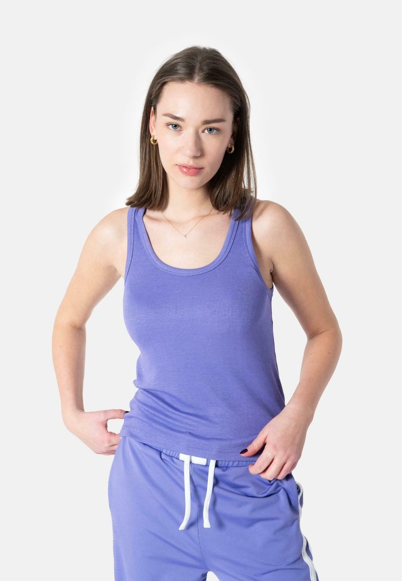 Lilla, ribbet tanktop med brede stropper, parret med matchende lilla joggebukser med hvite snorer og sidestriper.