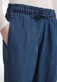 Joggers de denim azul con cintura elástica, detalles de cordón, bolsillos laterales y diseño de pierna recta, que presentan una textura suave.