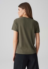 Olive green ribbed short-sleeve shirt, featuring a crew neckline and a relaxed fit, with soft texture and subtle stitching details.