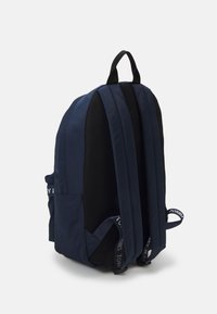 Granatowy plecak z siateczkowymi akcentami, wyściełanymi paskami i wzmocnionym uchwytem u góry; zawiera logo na pasku oraz wiele przegródek.